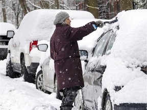 Carol Bishop clears snow off her car in the Notre-Dame-de-Grâce district of Montreal on Tuesday, Dec. 31, 2019.  The city of Montreal public health department is asking people to clear the snow off their vehicle first before starting it in order to avoid the risk of carbon-monoxide poisoning.