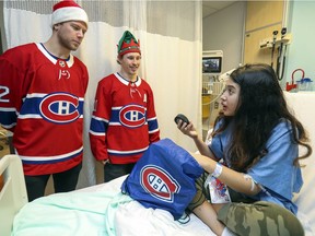 T.K., who preferred her full name not be used, pulls a puck out of gift bag given to her by Canadiens' Christian Folin, left, and Brendan Gallagher during the team's annual Christmas visit to the Montreal Children's Hospital.