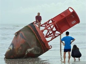 Beachgoers inspect a navigational marker that washed up on the beach last week in New Smyrna Beach, Fla., Saturday, Dec. 27, 2019. A Coast Guard spokesman said the marker originated in South Carolina. The marker seems to have been on a journey for about two years.  (Casmira Harrison/The Daytona Beach News-Journal via AP) ORG XMIT: FLDAY101