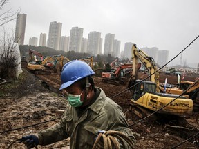 An electrician sets up wiring while workers drive excavators at the construction site of the first of now two field hospitals being built in Wuhan, Hubei Province, China.