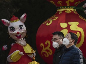 Chinese men wear protective masks as they walk by a decoration marking the Year of the Rat in a park after celebrations for the Chinese New Year and Spring Festival were cancelled by authorities on January 25, 2020 in Beijing, China.