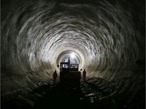 Workers walk past a digger in the partially completed Crossrail rail tunnel that will become Bond Street station on December 8, 2014 in London, England.