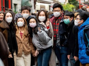 Pedestrians are seen wearing a surgical masks as they pose for a photograph in London's China Town on Saturday, Jan. 25, 2020. European airports from London to Moscow stepped up checks Wednesday on flights from the Chinese city at the heart of a new SARS-like virus that has killed 42 people and spread to the United States.