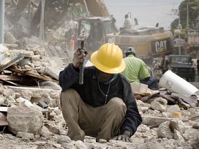 A man uses a hammer to break up concrete while heavy equipment is used to remove another fallen building in Port-au-Prince Jan. 26, 2010.