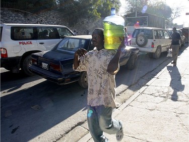 A man walks with a water jug filled with gasoline past cars waiting in line for gas on a street in Port-au-Prince, Haiti, on January 17, 2010.