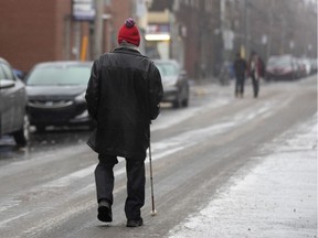 A visually impaired elderly man uses his white cane to follow the tire path on the street due to ice covered sidewalks in Montreal on Dec. 7, 2019.