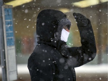 A commuter uses their hand to block blowing snow while waiting for a bus on Sherbrooke St. W. Friday morning.