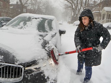 Cynthia Weinstein clears snow off her car on Beaconsfield Ave. Friday morning. Streets are being cleared, but plows are leaving some cars boxed in by windrows.