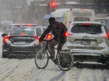 A cyclist navigates his way through traffic on Sherbrooke St. W. during Friday's storm. Sûreté du Québec were urging motorists to postpone non-essential travel or adapt their driving to accommodate slippery streets and poor visibility caused by blowing snow.