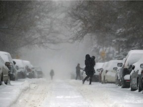 A woman carries a child across Hingston Ave. during Friday's snow storm in Montreal. As of 5 a.m. Friday, 10 to 15 to centimetres of snow had already fallen over the region since Thursday.