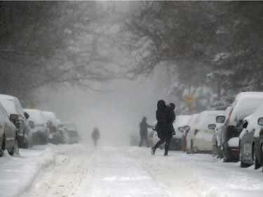 A woman carries a child across Hingston Ave. during Friday's snow storm in Montreal. As of 5 a.m. Friday, 10 to 15 to centimetres of snow had already fallen over the region since Thursday.