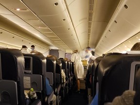 This picture provided by a passenger, Lolita Wiesner, on Feb. 21, 2020, shows medical personnel employees in protective gear serving breakfast and checking temperature for signs of fever to the Canadians evacuated from the Diamond Princess cruise ship, inside a charter plane on their way back from Japan to Canadian Forces Base Trenton on Feb. 20.