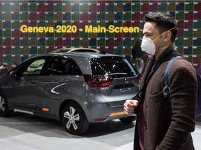 A man wearing a mask stand near a car on February 28, 2020 at the Geneva International Motor Show which has been cancelled due to the Covid-19 epidemic.