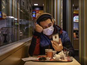 A man wears a protective mask as he looks at his mobile phone while eating at a McDonald's restaurant in a residential neighbourhood on Saturday, Feb. 8, 2020, in Beijing.