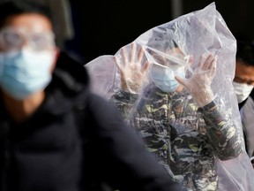 A passenger wearing a mask and covered with a plastic bag walks outside the Shanghai railway station in Shanghai, China, as the country is hit by an outbreak of a new coronavirus, Sunday, Feb. 9, 2020.