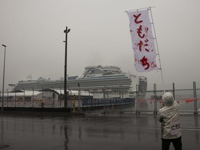 A man waves a banner that reads in Japanese "Friends" near the quarantined Diamond Princess cruise ship Sunday, Feb. 16, 2020, in Yokohama, near Tokyo. The federal government says it will evacuate Canadians quarantined aboard a cruise ship docked in Japan.