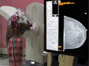 A patient is seen through the glass as she undergoes a mammogram.