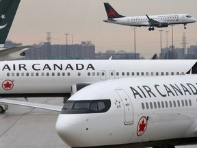 Two Air Canada Boeing 737 MAX 8 aircrafts are seen on the ground as Air Canada Embraer aircraft flies in the background at Toronto Pearson International Airport in Toronto in March 2019.