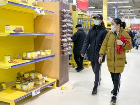 Shoppers wearing masks walk by depleted shelves at the Maxi store in Pointe Claire, west of Montreal Friday March 13, 2020.