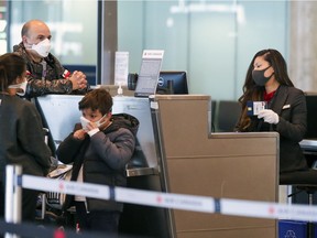 An Air Canada passenger service representative wears a mask and gloves while checking in a departing family at Trudeau Airport in Montreal Monday March 16, 2020.