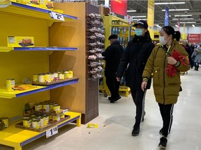 Shoppers wearing masks walk by depleted shelves at the Maxi store in Pointe-Claire on March 13, 2020.