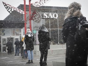 Customers brave the falling snow as they wait in line to enter the SAQ store at Marché Jean-Talon on March 23, 2020.
