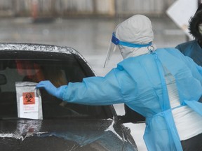 A woman, who would administer a nasal swab, removes an envelope with personal information in it and a vessel to put material from the swab in it. This was part of a screening process at a COVID-19 drive-through screening clinic in the Côte-St-Luc area of Monreal in Montreal Sunday, March 29, 2020.