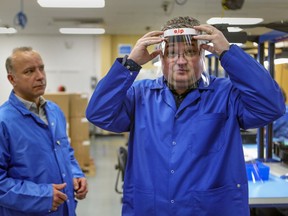 Éric Pouin, director manufacturing engineering at E2IP Technologies, watches as Steve Séguin, vice-president, operations, and engineering, tries on a visor for health care workers that the company has developed in response the coronavirus pandemic, at their plant in Lachine.