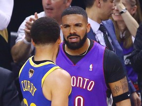 Rapper Drake and Stephen Curry #30 of the Golden State Warriors exchange words during a timeout in the first quarter during Game One of the 2019 NBA Finals between the Golden State Warriors and the Toronto Raptors at Scotiabank Arena on May 30, 2019 in Toronto, Canada.