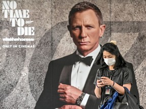 A woman wearing a facemask amid fears of the spread of the COVID-19 novel coronavirus walks past a poster for the new James Bond movie "No Time to Die" in Bangkok on February 28, 2020. - The new coronavirus has peaked in China but could still grow into a pandemic, the World Health Organization warned, as infections mushroom in other countries. (Photo by Mladen ANTONOV / AFP)