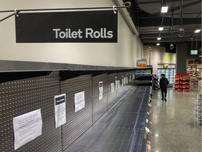 A shopper passes empty shelves usually stocked with toilet paper in a supermarket in Melbourne, Australia on March 5, 2020. - COVID-19 coronavirus fears have triggered runs on several products, including hand sanitizers and face masks, with images of shoppers stacking trolleys with toilet rolls spreading on social media.