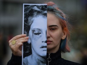 An activist holds a printed half face picture showing a victim of domestic violence during a protest in Bucharest on March 4, 2020. "Isolation works to the advantage of abusers, allowing them to exercise greater power and control over their victims," Cassandra Richards says.