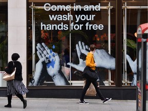 Pedestrians pass a cosmetics shop advertising free hand washing facilities in store in Liverpool, northwest England, on March 11, 2020. "As the situation intensifies day by day, and even moment by moment, it is imperative that our understanding of it and our reaction to it keep pace," Fariha Naqvi-Mohamed writes.