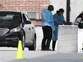 Workers in protective gear, process a patient in a car at one of the first drive through testing facilities for Coronavirus (COVID-19) in a parking lot outside the University of Utah's Sugar House Health Clinic  in Salt Lake City, Utah on March 16,  2020.