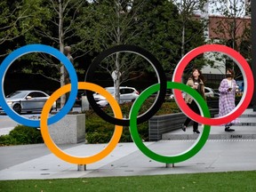 People take pictures of the Olympic Rings outside the closed Japan Olympic Museum in Tokyo on Friday, March 27, 2020, three days after the historic decision to postpone the 2020 Tokyo Olympic Games.