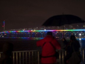 A man takes photographs of the Samuel Champlain Bridge lit up in the colours of the rainbow in solidarity with health-care workers in Montreal March 29, 2020.