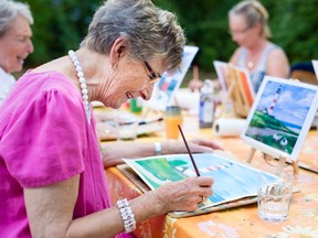 Side view of a happy senior woman smiling while drawing as a recreational activity or therapy outdoors together with the group of retired women.