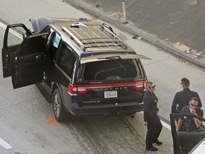 Los Angeles police officers stand after a pursuit of a stolen hearse with with a casket and body inside on Interstate 110 in South Los Angeles Thursday, Feb. 27, 2020.  The hearse was stolen from outside a Greek Orthodox church in East Pasadena on Wednesday night. The Los Angeles County Sheriff's Department says one person is in custody.