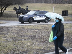 A masked pedestrian sports and umbrella to shield from the Covid-19 and the rain, while Montreal police stand near George-Etienne Cartier monument to emphasize social distancing on Thursday April 2, 2020. (Pierre Obendrauf / MONTREAL GAZETTE) ORG XMIT: 64207 - 2803