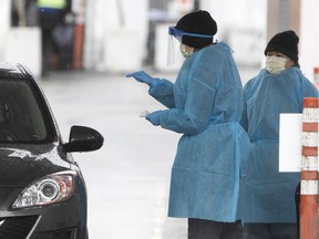 Health-care workers give instructions to a patient as they carry out drive-through tests for COVID-19 at Cavendish Mall on Monday, March 30, 2020.