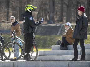A Montreal police officer issues a verbal warning to a group of friends at Sir Georges-Etienne Cartier monument April 20, 2020.