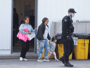 Asylum seekers follow a RCMP officer after being processed for crossing the border from New York into Canada at Roxham Road in Hemmingford, Quebec, March 19, 2020.