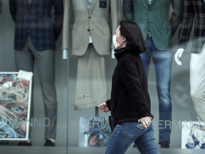 A masked pedestrian walks past a storefront in Toronto