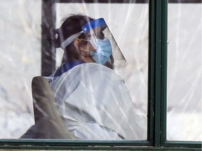 A worker in personal protective equipment sits near a window at Résidence Herron in Dorval.