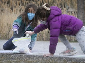 Wearing their masks, seven-year-old Salix, left, passes a bag of chalk to her best friend, six-year-old Sloan, at Jarry Park on Monday, May 11, 2020. Many Quebec kids went back to school that day, but Montreal kids are still at home during the COVID-19 pandemic.