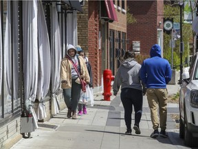 People squeeze against a storefront to allow distancing with other pedestrians walking on Ste-Anne St. in Ste-Anne-de-Bellevue, west of Montreal, on May 12, 2020.