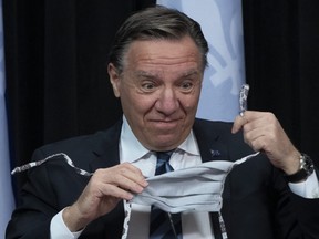 Quebec Premier Francois Legault reacts as he pulls off his hand-made mask during a news conference on the COVID-19 pandemic, Tuesday, May 12, 2020 at the legislature in Quebec City.