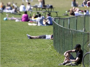 A man reads alone, away from others in a busy Jeanne-Mance Park on Monday, May 18, 2020.