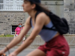 A woman wearing a mask watches as a cyclist not wearing one passes by on des Pins Ave.