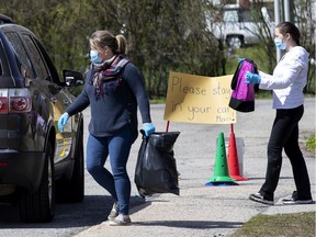 Staff load cars as parents pickup their children's personal belongs at a drive through type setup at St. John Fisher elementary school in Montreal, on Wednesday, May 6, 2020.